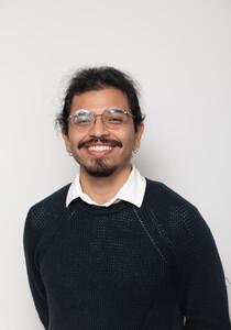 Headshot of smiling man with glasses, hair tied back, black sweater and white collared shirt