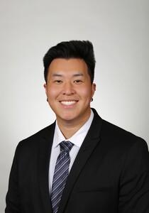 Smiling professional headshot photograph wearing dark suit and striped tie, light gray background